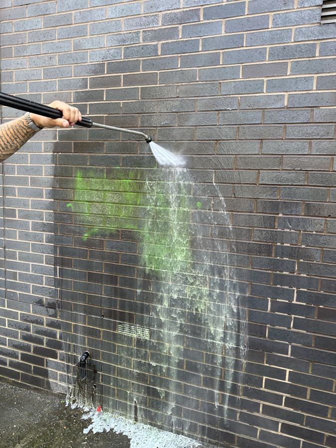 Green spray paint graffiti being washed off brickwork